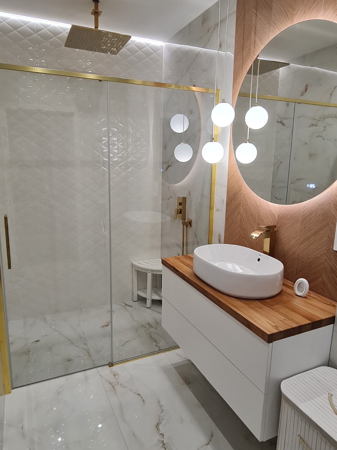 Elegancka łazienka: kabina prysznicowa z deszczownicą, umywalka nablatowa na drewnianym blacie, okrągłe lustro z podświetleniem i designerskie lampy.
