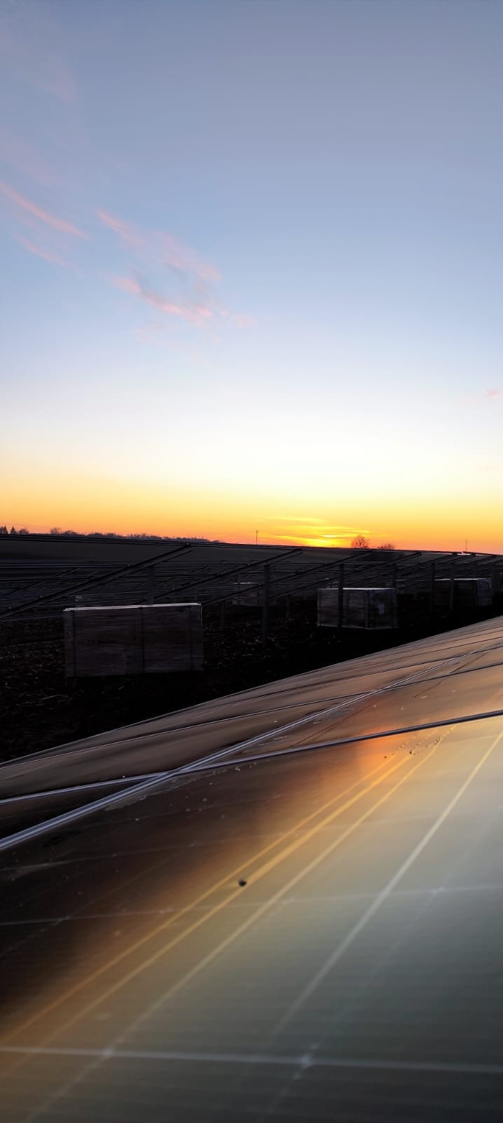 Panele słoneczne odbijające zachodzące słońce na tle pola i nieba o zmierzchu.