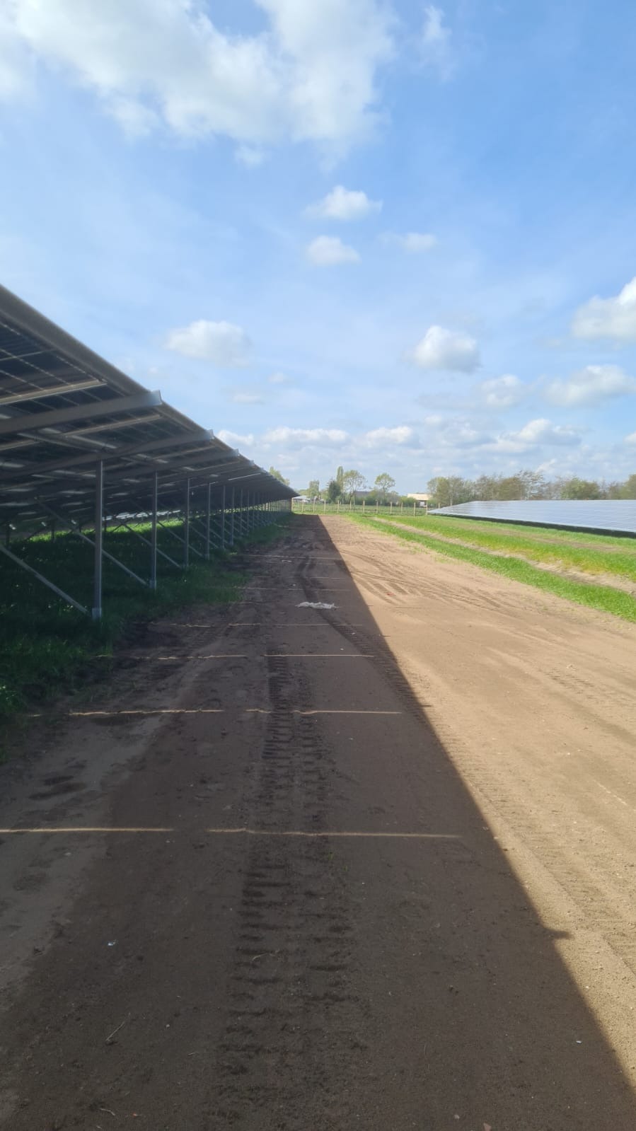 Rząd paneli fotowoltaicznych na metalowej konstrukcji, widok z dołu, z ziemi, ślady opon na ziemi.