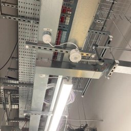 Andrzej Korda - Sufit z zamontowanymi metalowymi korytkami kablowymi, oświetleniem LED i czujnikiem ruchu PIR. Widoczne przewody w kolorowych izolacjach.