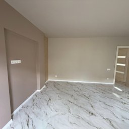 Andrzej Serwis - Jasne, świeżo pomalowane wnętrze z marmurową podłogą i beżowymi ścianami. Widoczne gniazdka elektryczne i białe listwy przypodłogowe. Nowoczesne drzwi w tle.