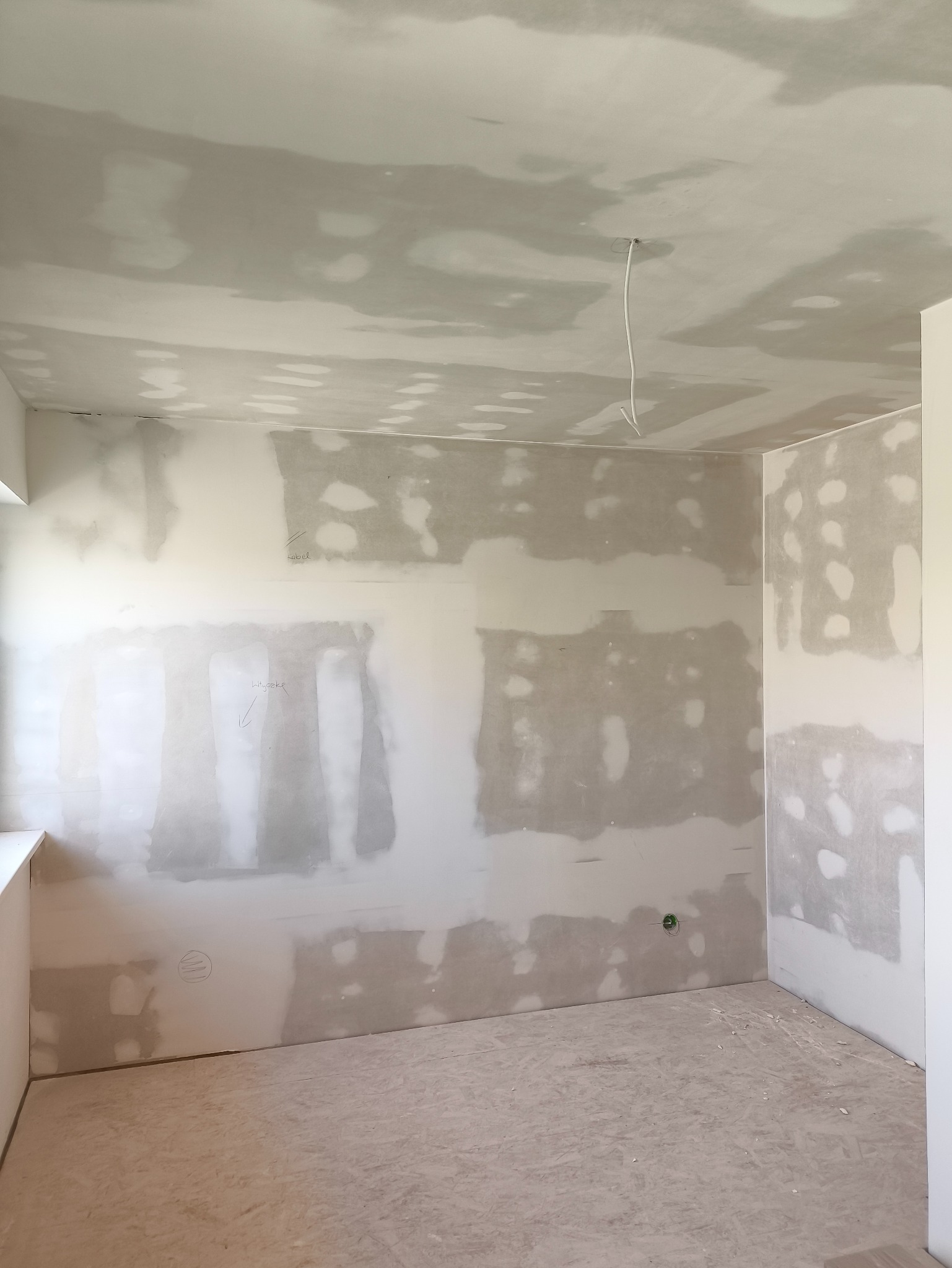 Pokój w trakcie szpachlowania ścian i sufitu, widoczne ślady po łatach gipsowych, surowy stan wykończenia wnętrza, przygotowanie do dalszych prac remontowych.
