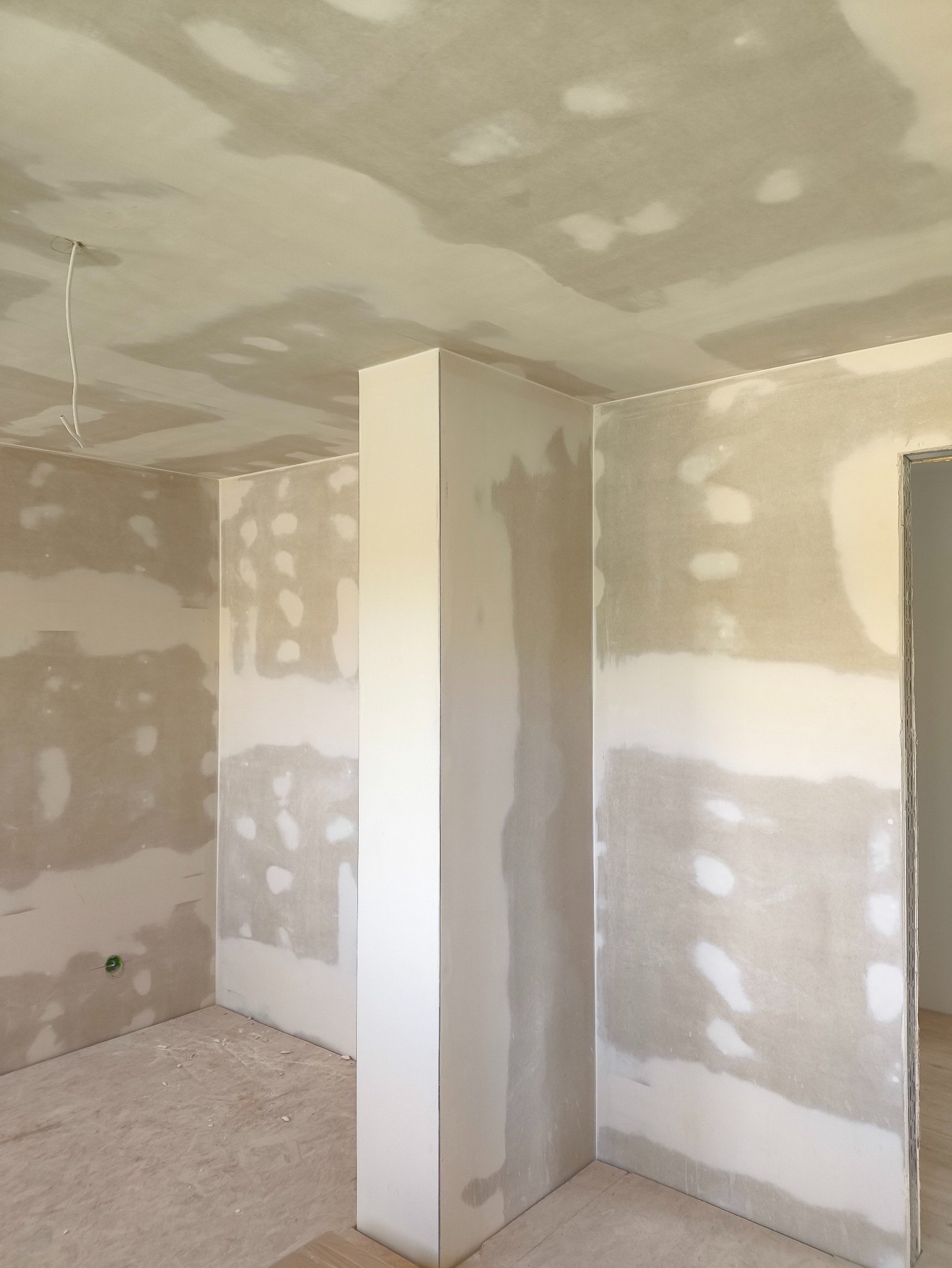 Wnętrze w trakcie szpachlowania: sufit i ściany pokryte gładzią gipsową, widoczne łączenia płyt karton-gips. Przygotowanie do malowania w nowym domu.