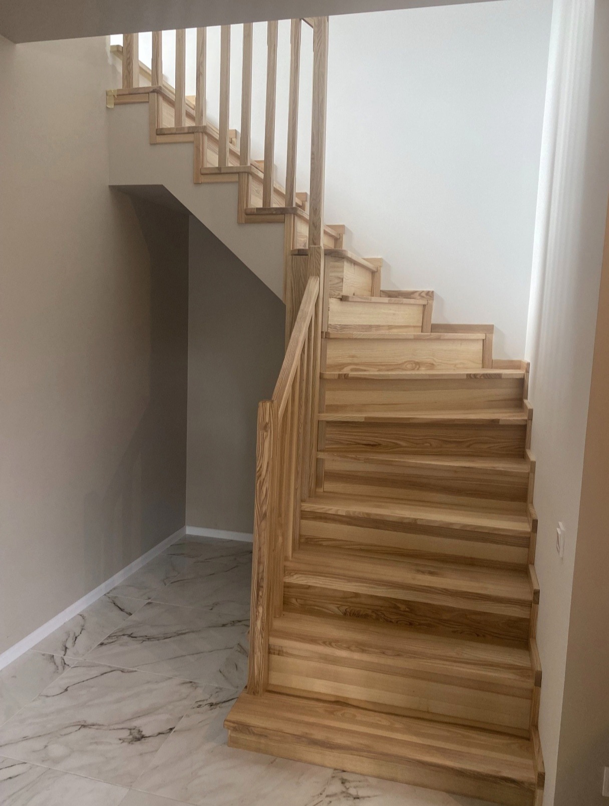 Drewniane schody z balustradą, jasne drewno, marmurowe płytki podłogowe. Widok z dołu, naturalne oświetlenie, minimalistyczny design.