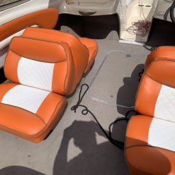 ZAKŁAD USŁUGOWO PRODUKCYJNY WOJCIECH SULKOWSKI - Tapicerowane, pomarańczowo-białe siedzenia w łodzi motorowej z czarną liną. Widoczny fragment kokpitu i kierownica. Czyste, jasne oświetlenie.
