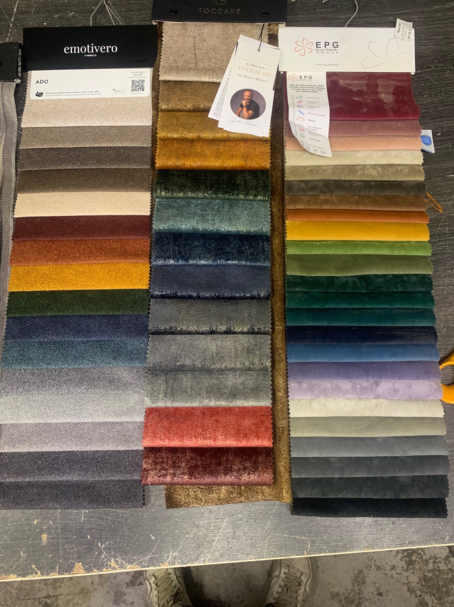 Paleta różnorodnych próbek tkanin tapicerskich o różnych fakturach i kolorach, prezentowanych w trzech zestawach. Widoczne oznaczenia producentów i nazwy kolekcji.