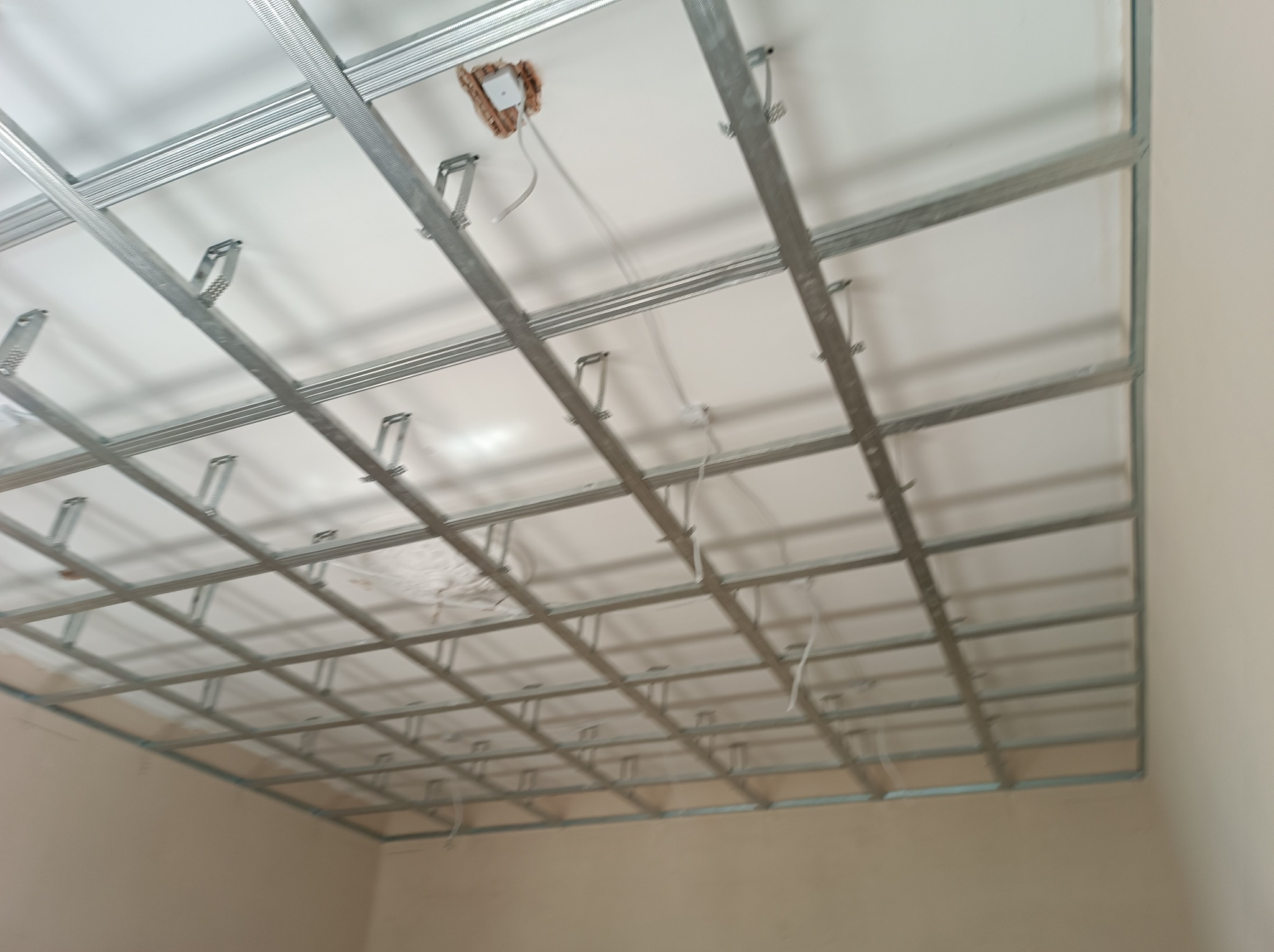 Metalowa konstrukcja sufitu podwieszanego z płyt kartonowo-gipsowych, widoczne przewody elektryczne w puszce, częściowo zamontowane białe płyty