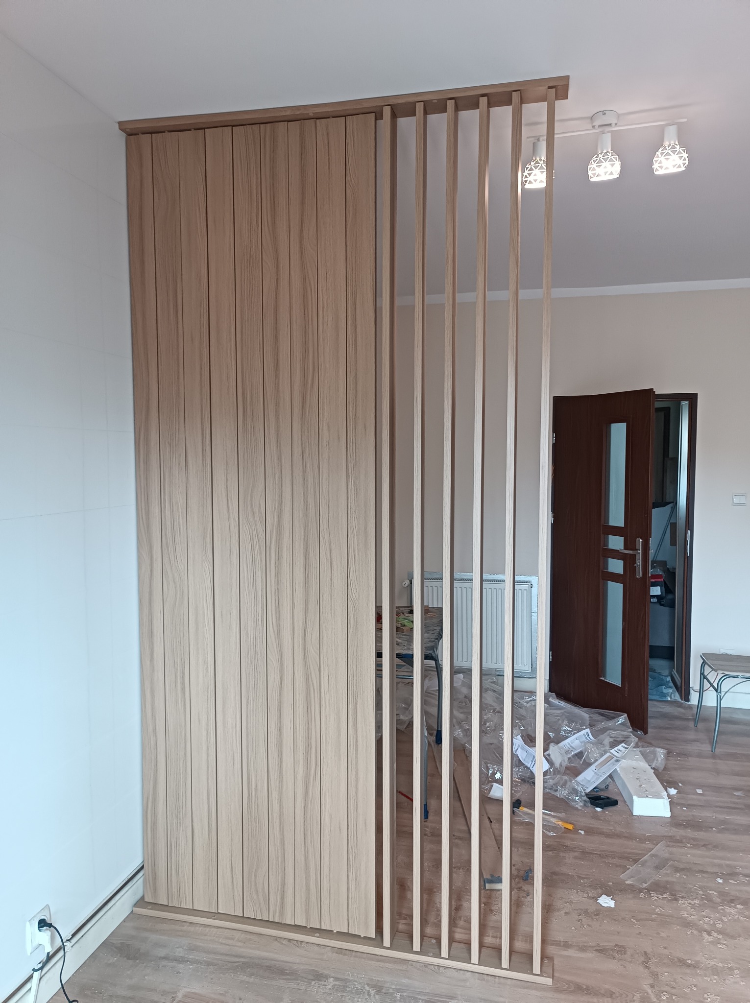 Montaż drewnianej ścianki działowej z pionowych listew i paneli, widoczne niedokończone prace i elementy wykończeniowe na podłodze.