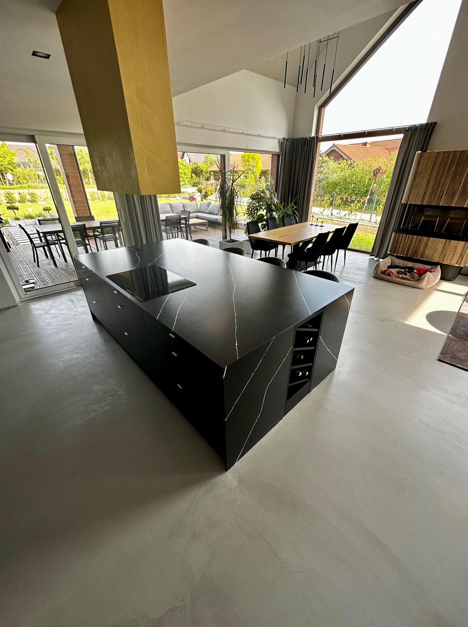 Czarna wyspa kuchenna z białymi żyłami na posadzce w nowoczesnym domu z dużymi oknami.