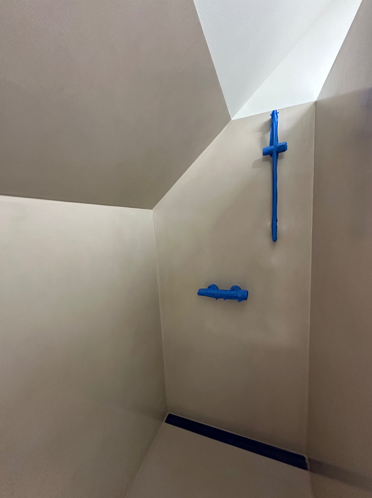 Ściany i sufit w łazience pokryte mikrocementem w odcieniach szarości, zabezpieczone niebieską taśmą malarską przed montażem armatury prysznicowej.