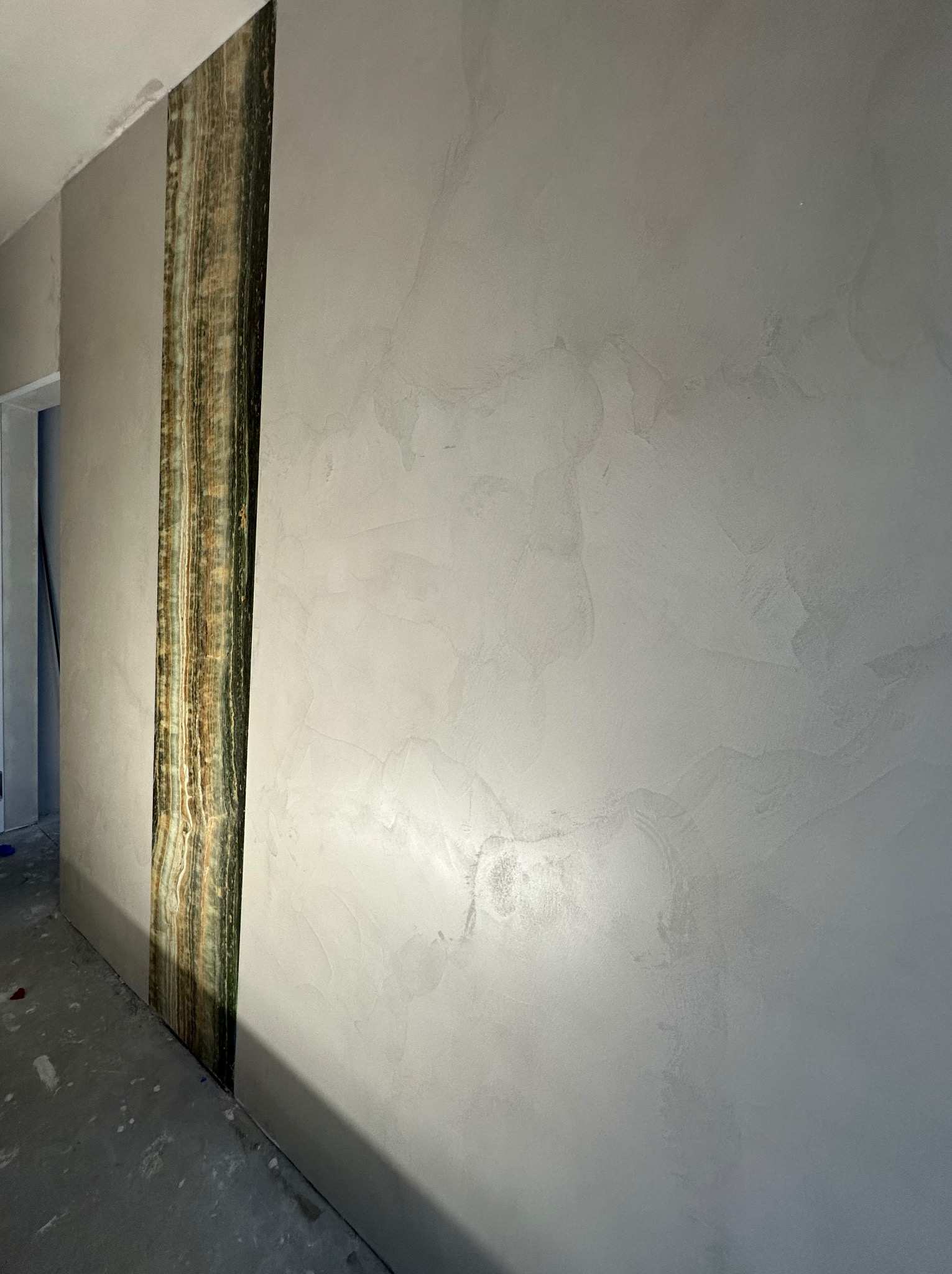 Ściana z dekoracyjną powłoką imitującą kamień, z pionowym pasem z efektem onyksu. Szara, gładka powierzchnia z subtelnymi wzorami. Wykończenie wnętrza.