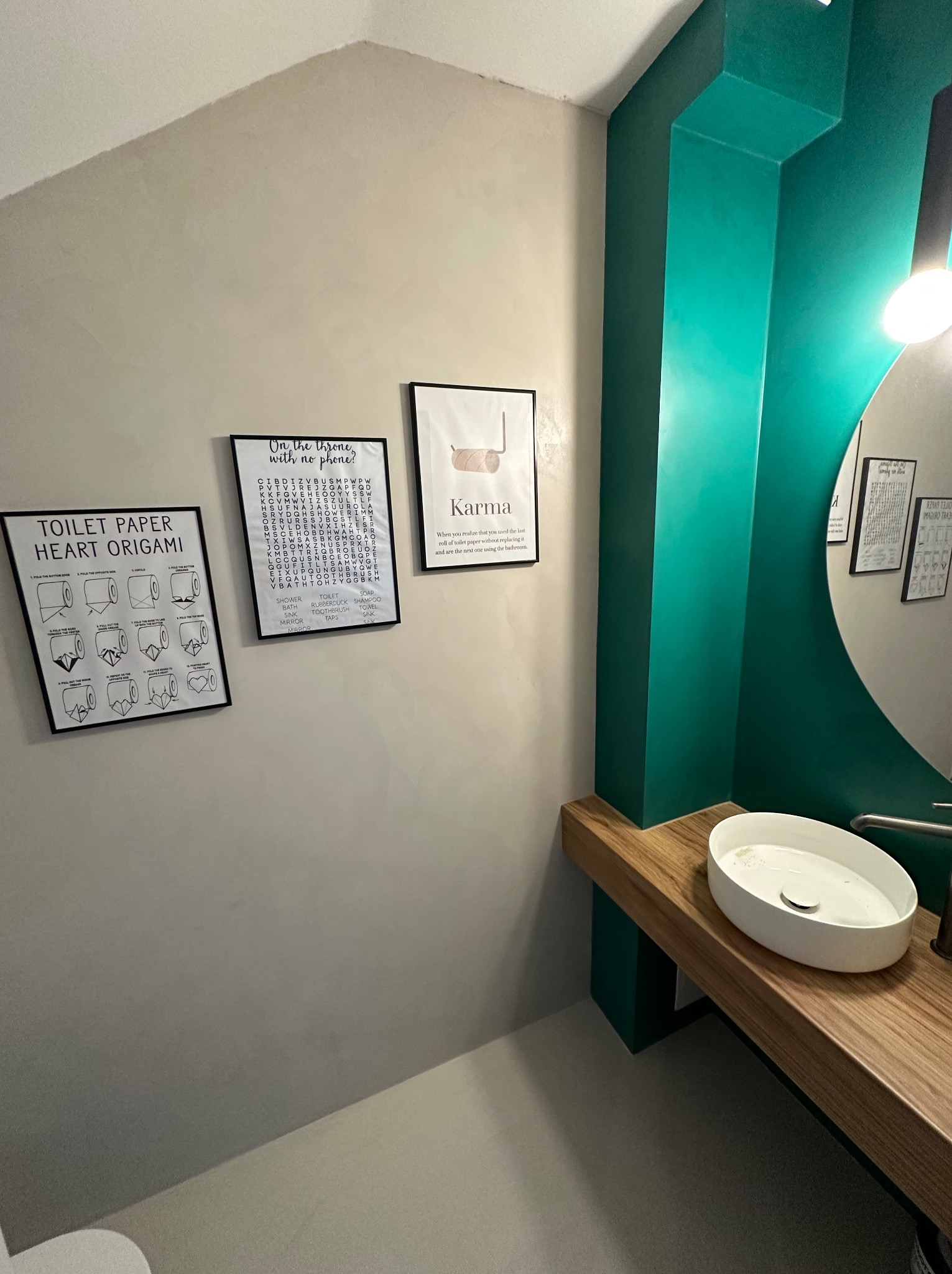 Wykończona łazienka z mikrocementem na ścianach i podłodze, z umywalką na drewnianym blacie i dekoracyjnymi plakatami na ścianie. Minimalistyczny design.