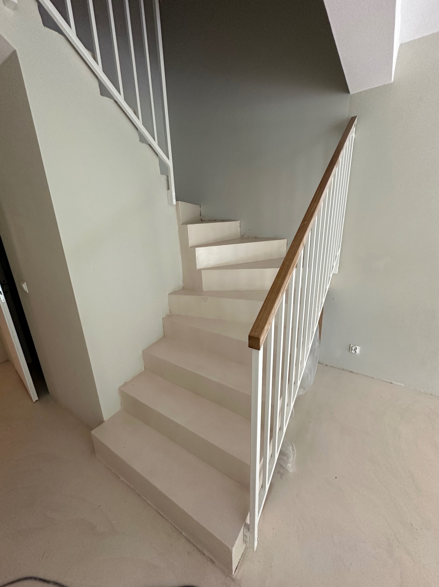 Jasne schody z białymi barierkami i drewnianym poręczą, wykończone w jednolitej, jasnej tonacji, z widoczną strukturą posadzki. Minimalistyczny design.