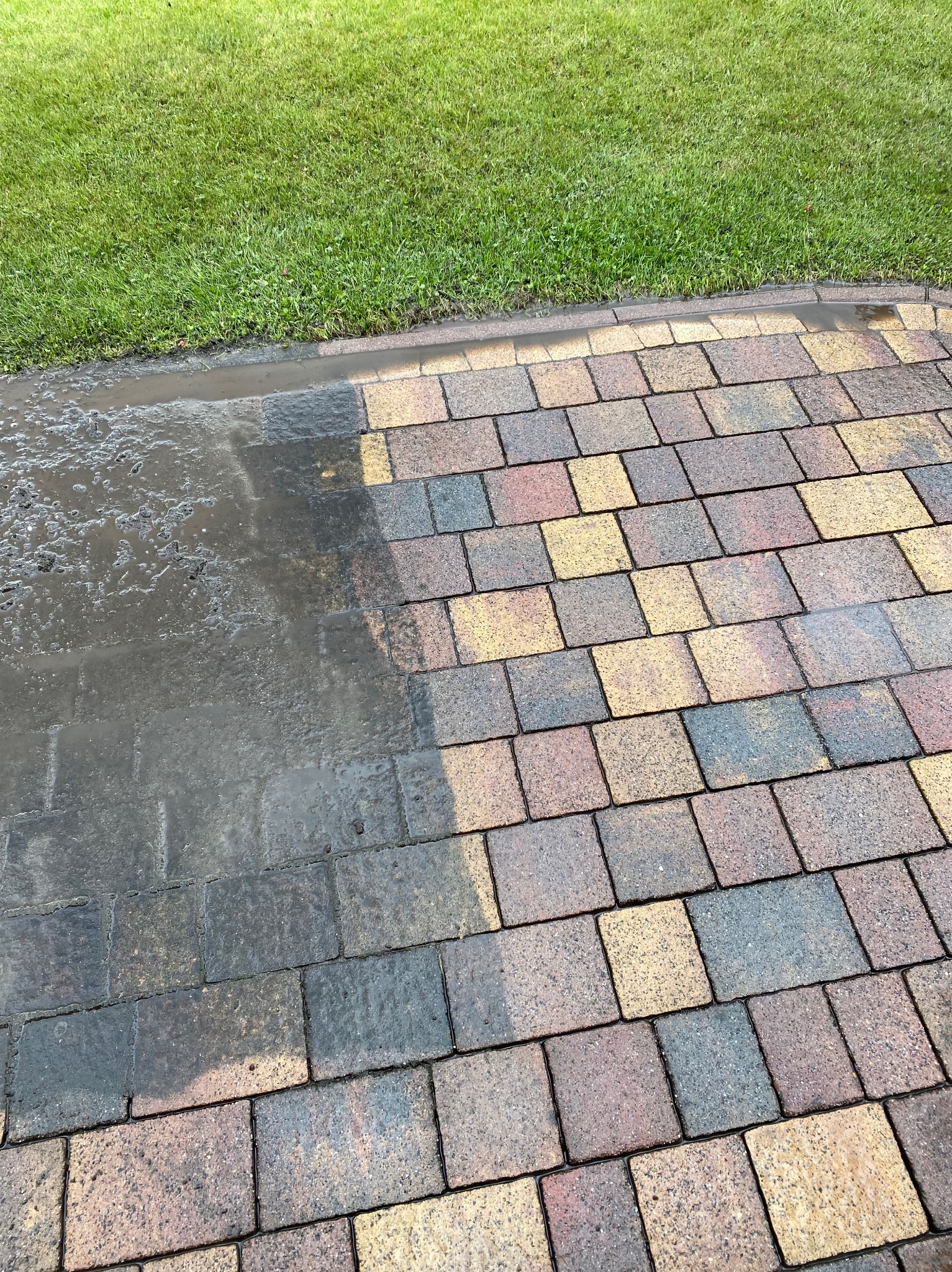 Kostka brukowa po częściowym czyszczeniu pod ciśnieniem, z widoczną różnicą w kolorze i czystości. Po lewej mokra, ciemna, po prawej sucha, w odcieniach brązu i żółci.