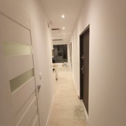 SinggaDruk Filip Sinulingga - Sztuka na każdej ścianie - Biały korytarz po malowaniu z widokiem na kuchnię. Nowoczesne drzwi z przeszkleniami i ciemne drzwi wejściowe. Świeżo pomalowane ściany i sufit.