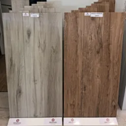 Prezentacja dwóch rodzajów płytek gresowych imitujących drewniane panele podłogowe: Astone Silver (szare) i Bricolla Marrone (brązowe), o wymiarach 120x20, z ekspozycji producenta PAFIceramic.