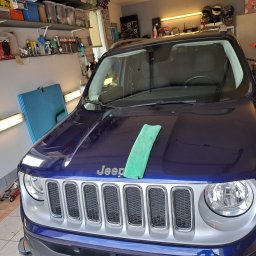Drobne naprawy pojazdów, konserwacja ,sprzątanie Adam Wołoszyn - Niebieski Jeep Renegade w garażu, z zieloną ściereczką mikrofibry na masce, przygotowany do czyszczenia lub polerowania.