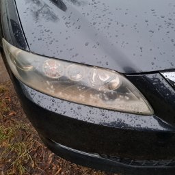 Drobne naprawy pojazdów, konserwacja ,sprzątanie Adam Wołoszyn - Przedni reflektor samochodu z widocznymi śladami zużycia i kroplami wody na karoserii, sfotografowany w pochmurny dzień.