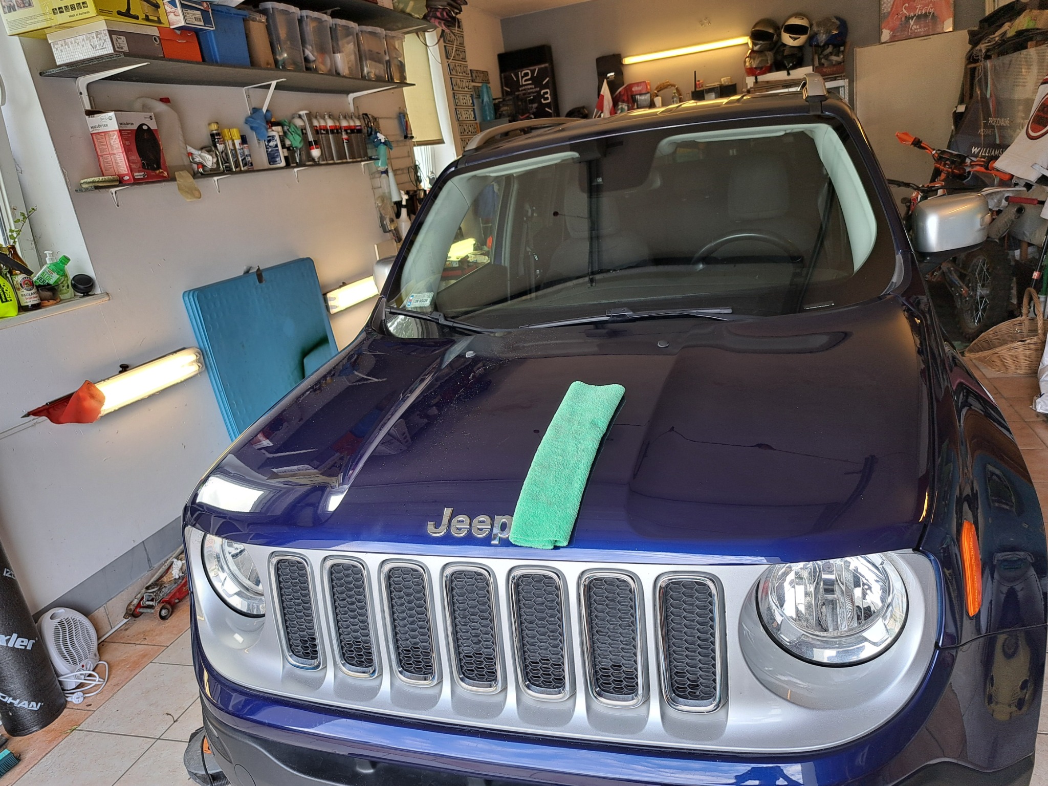 Niebieski Jeep Renegade w garażu, z zieloną ściereczką mikrofibry na masce, przygotowany do czyszczenia lub polerowania.