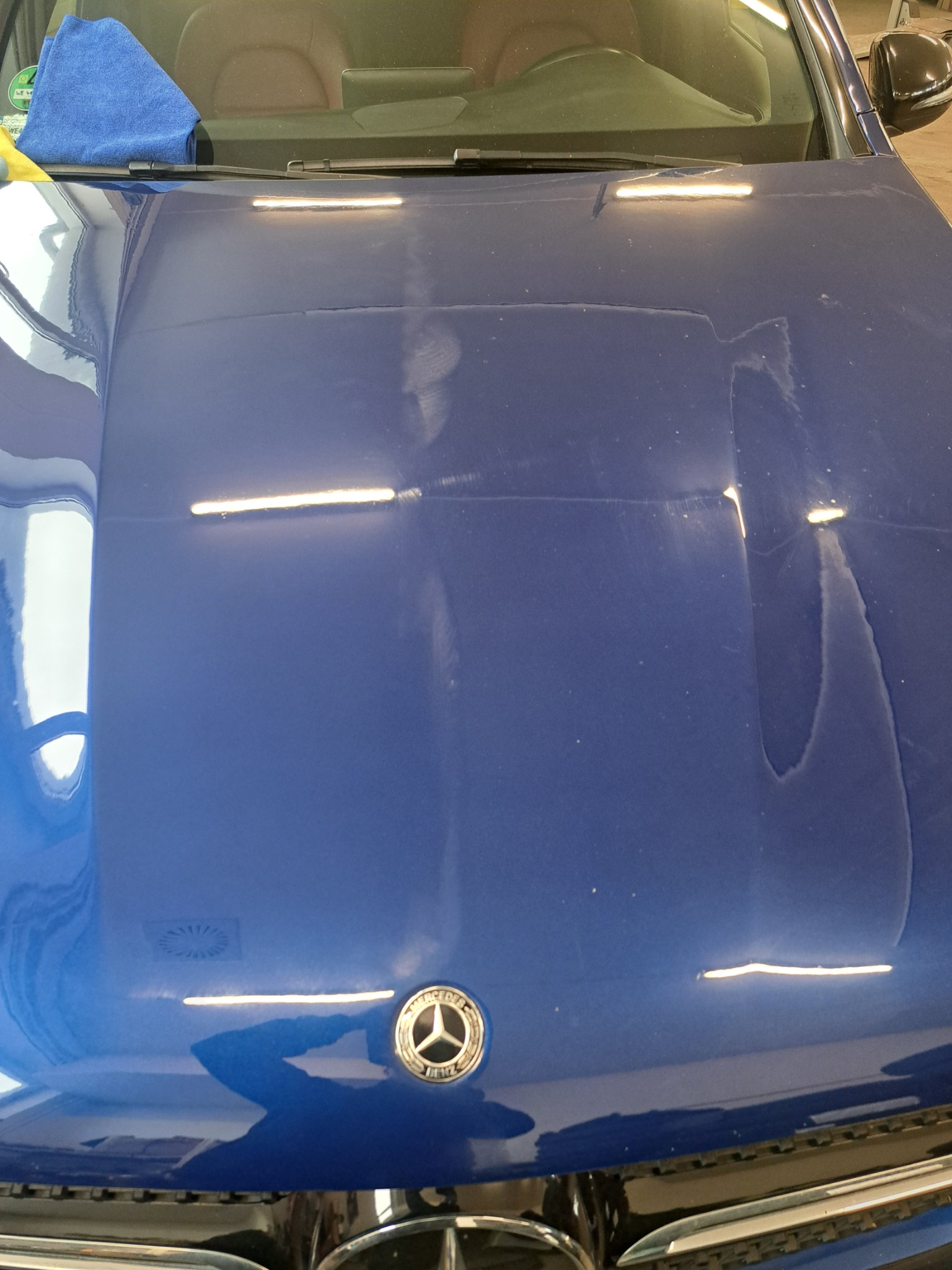Niebieski Mercedes z widocznymi śladami wody na masce, przygotowywany do polerowania. Ściereczka z mikrofibry na przedniej szybie.