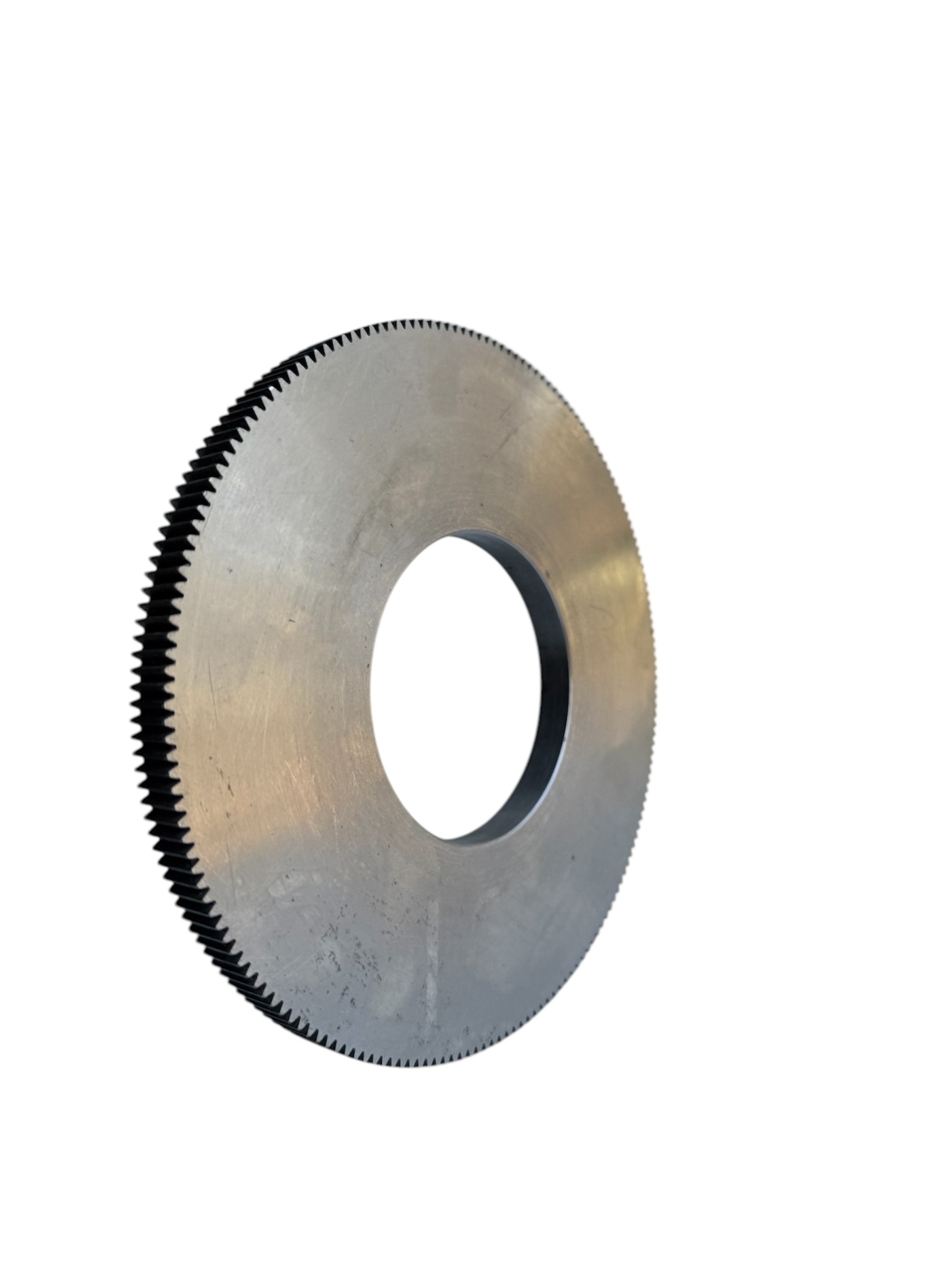 Metalowa tarcza z zębatym obrzeżem i centralnym otworem, widoczna pod kątem, ukazująca ślady obróbki i niewielkie zarysowania na powierzchni.