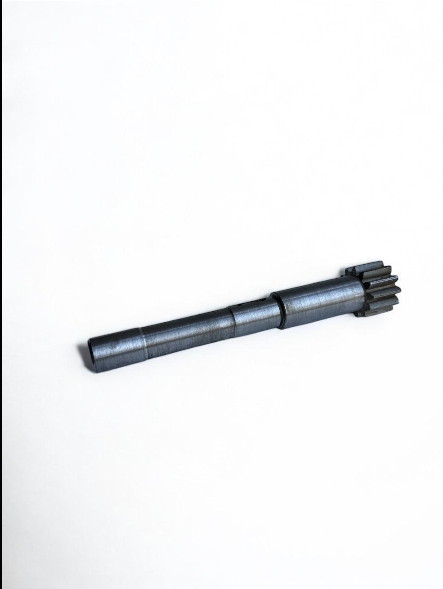 Metalowy wałek z zębatką na końcu, leżący na białym tle. Widoczne delikatne ślady obróbki na powierzchni.