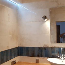 Asrem - Wykończona łazienka z białymi i niebieskimi płytkami, owalną umywalką i lustrem z oświetleniem. W lustrze odbija się osoba robiąca zdjęcie.