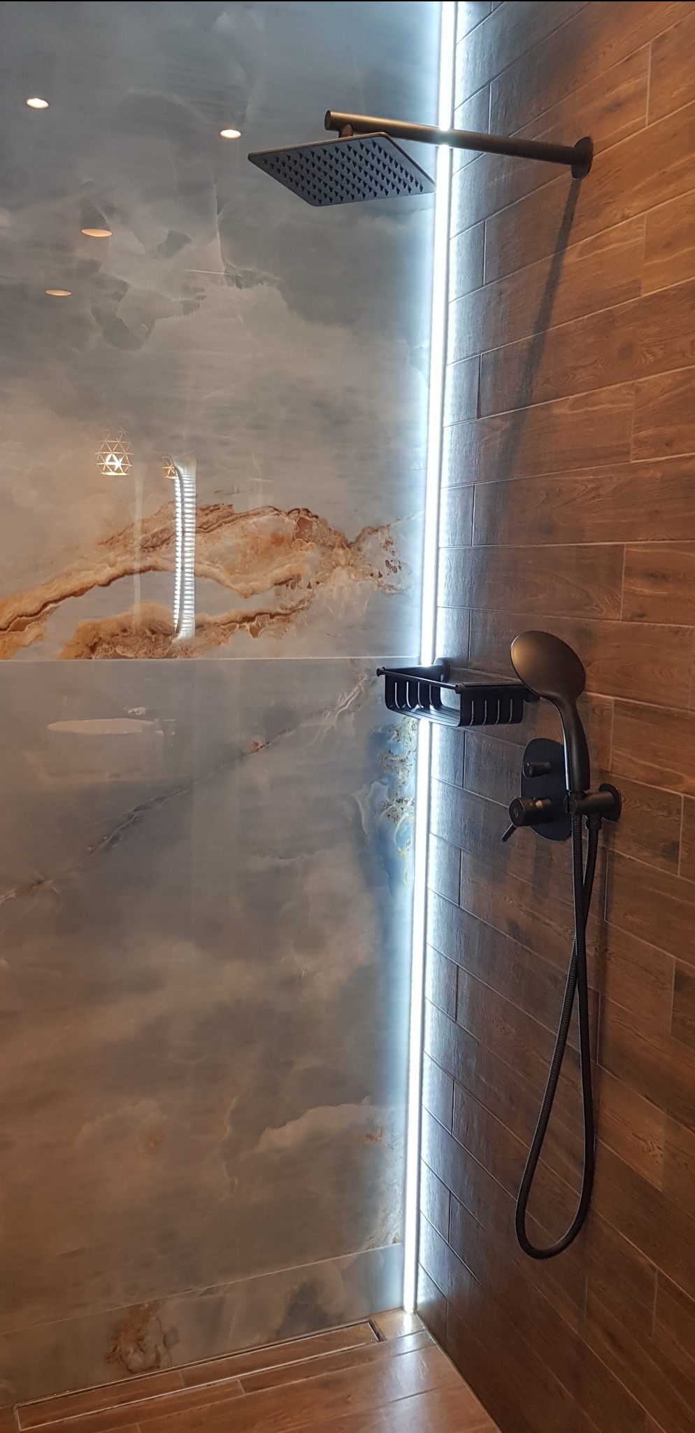Nowoczesna kabina prysznicowa z deszczownicą i oświetleniem LED. Ściany wyłożone płytkami imitującymi marmur i drewno. Czarna armatura.