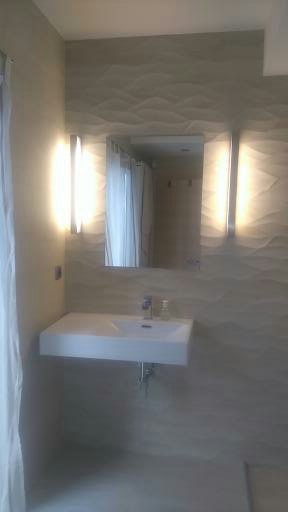 Minimalistyczna łazienka z białą, prostokątną umywalką, podświetlanym lustrem i dekoracyjną, falistą strukturą ściany w odcieniach beżu.