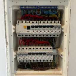 Rozdzielnica elektryczna Eaton w białej obudowie, z widocznymi bezpiecznikami, przewodami i elementami montażowymi. Ujęcie z bliska, detale instalacji.