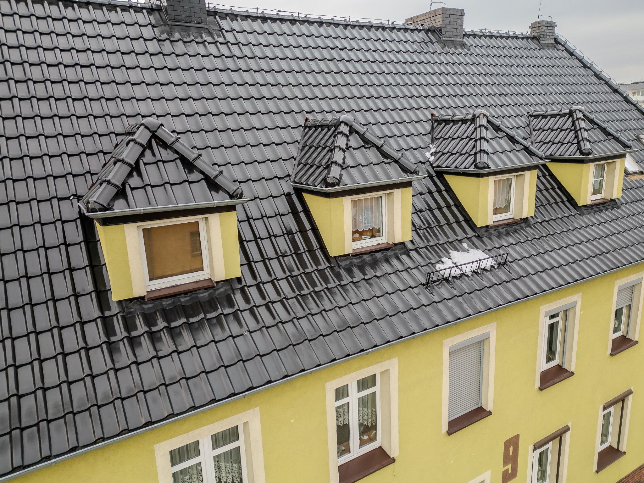 Czarny, błyszczący dach z dachówki ceramicznej na żółtym budynku z lukarnami, widok z góry.