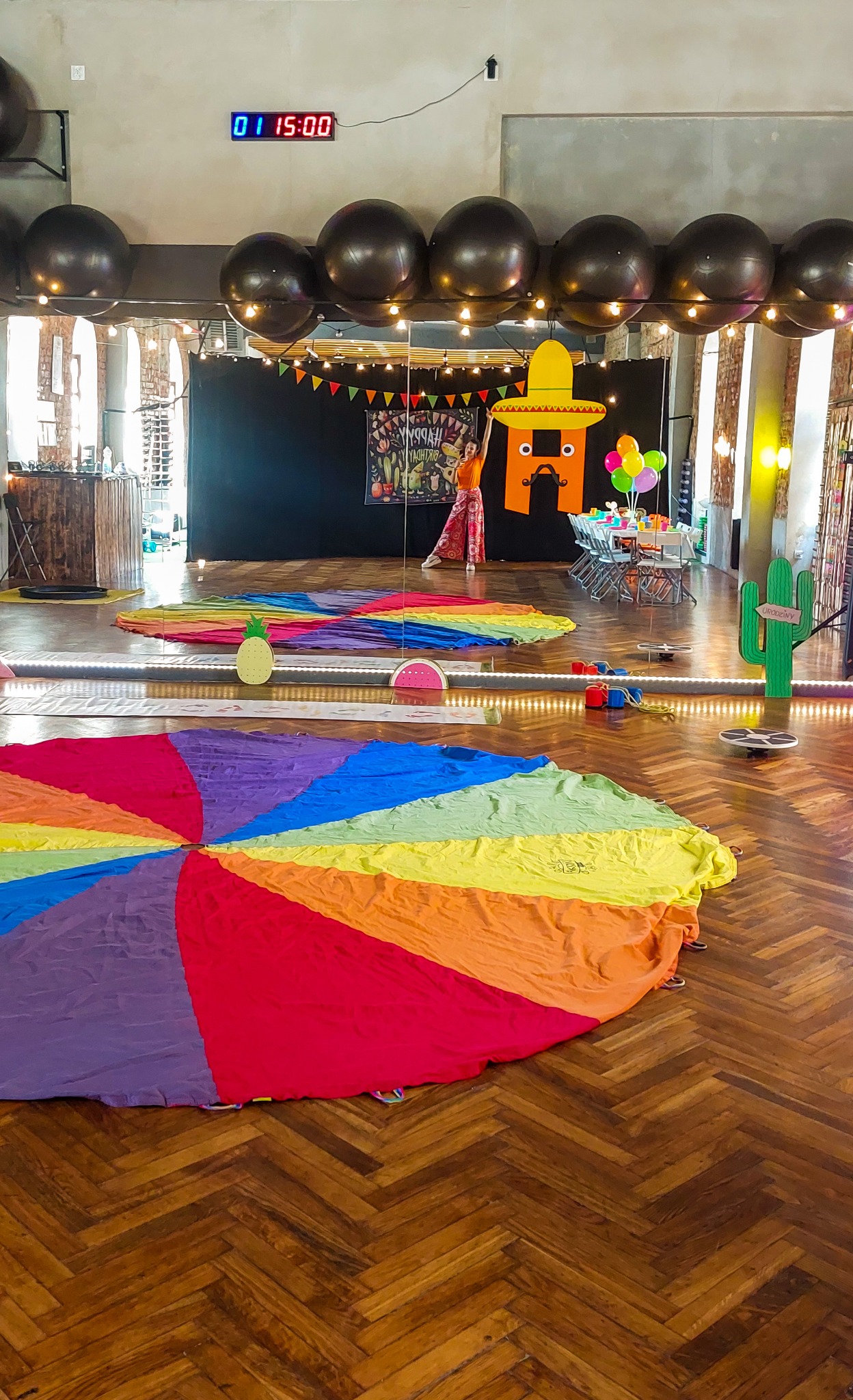 Kolorowa chusta animacyjna rozłożona na parkiecie w Krotoszynie, przygotowana do zabaw z dziećmi podczas urodzinowej imprezy, w tle dekoracje i animator w kostiumie.