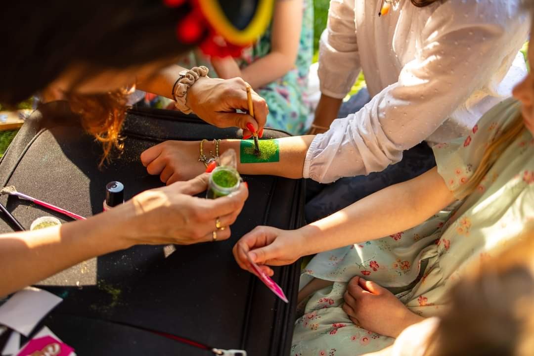 Malowanie farbami na skórze dziecka podczas imprezy plenerowej, widoczna zielona farba i pędzel w dłoni animatora.