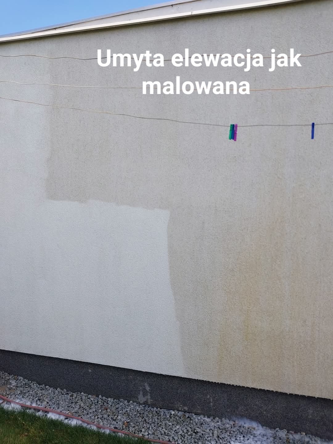 Fragment elewacji budynku z widoczną różnicą w kolorze po częściowym oczyszczeniu, na sznurku wiszą klamerki, a u dołu widoczny kamienny cokół i trawa.