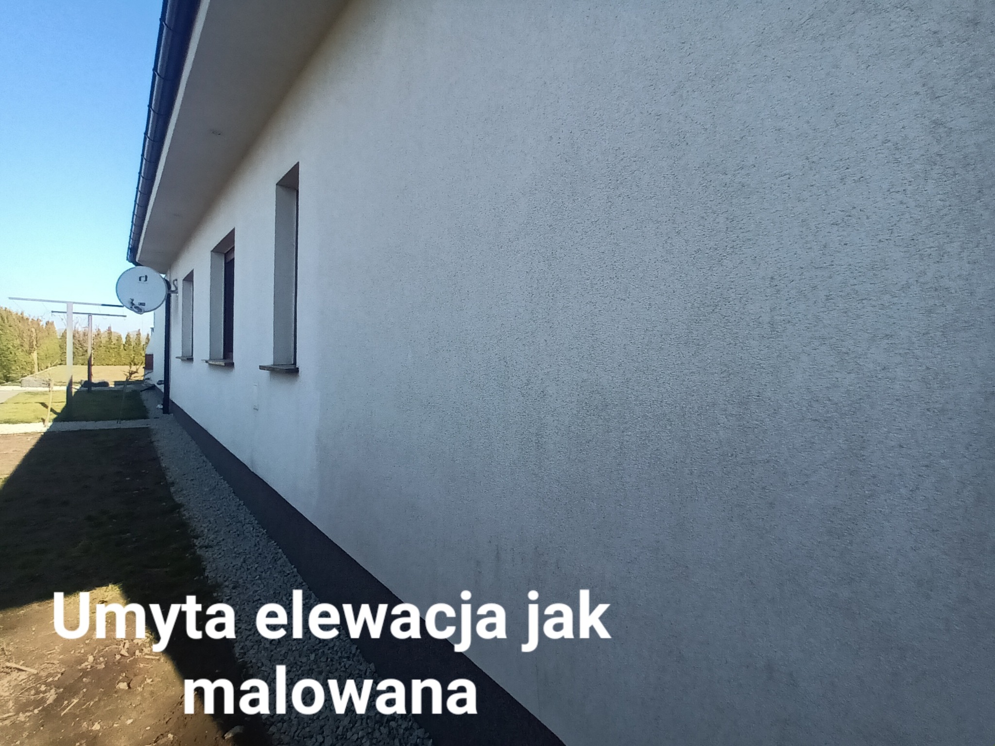 Jasnoszara, umyta elewacja budynku jednorodzinnego z widoczną anteną satelitarną i kamienną opaską przy gruncie.