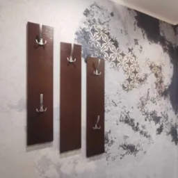 Dekoracyjna ściana z efektem spękań i wzorem kwiatowym, uzupełniona trzema wieszakami na ubrania z brązowego drewna z metalowymi haczykami.