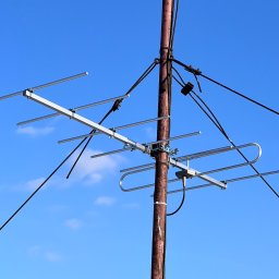 Antenka - Antena telewizyjna zamontowana na rdzewiejącym metalowym słupie, widoczna na tle błękitnego nieba z delikatnymi obłokami.