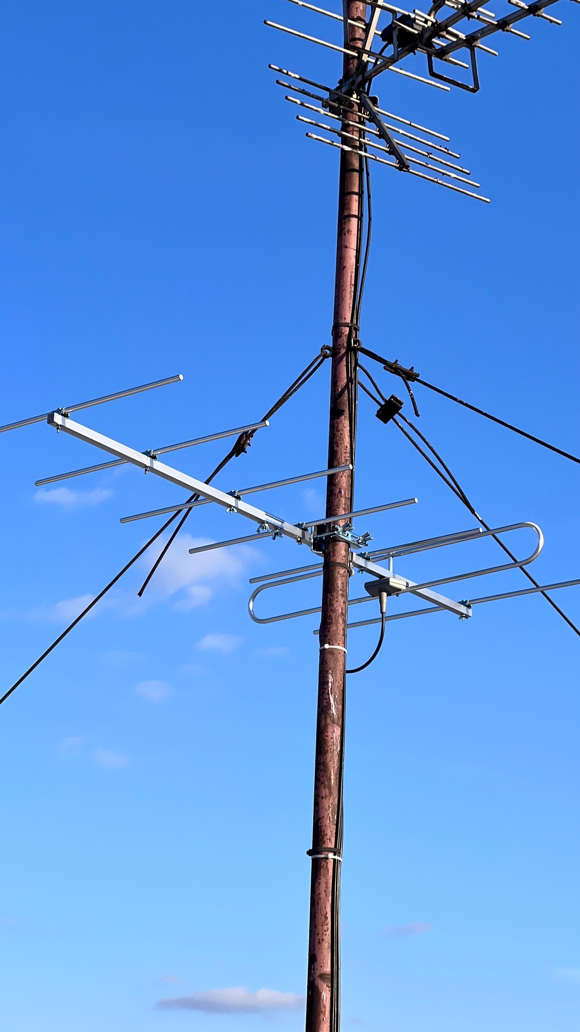 Antena telewizyjna zamontowana na rdzewiejącym metalowym słupie, widoczna na tle błękitnego nieba z delikatnymi obłokami.