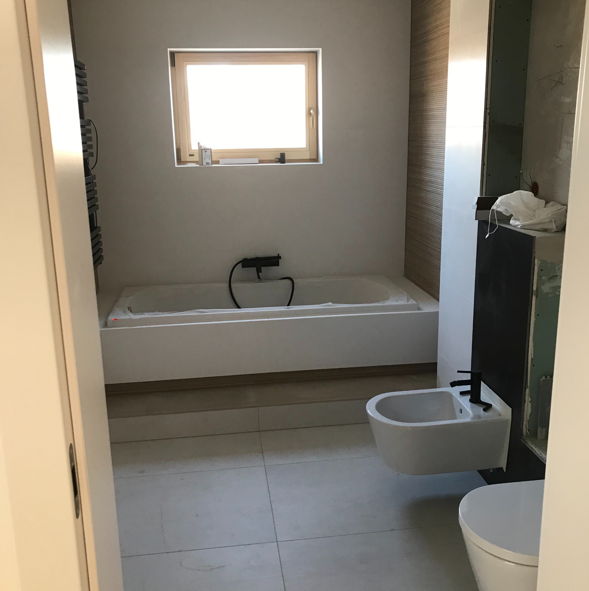 Wnętrze łazienki w trakcie wykańczania: wanna obudowana płytami, zamontowane bidet i toaleta, widoczna instalacja wodna, fragment ściany z płytą kartonowo-gipsową.