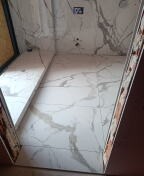 Wyłożona białymi płytkami imitującymi marmur wnęka prysznicowa z zamontowanym odpływem liniowym. Widoczne niedokończone obramowanie wnęki.