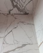 Ściana i podłoga wyłożone wielkoformatowymi płytkami imitującymi biały marmur z szarymi żyłami, widoczny odpływ liniowy w podłodze.