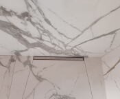 Biała łazienka wykończona wielkoformatowymi płytami imitującymi marmur, z widocznym odpływem liniowym w strefie prysznica.