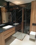 Nowoczesna łazienka z kabiną prysznicową typu walk-in, umywalką nablatową na drewnianej szafce z ciemnym blatem, lustro w czarnej ramie i czarne płytki imitujące marmur na ścianach.