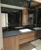 Nowoczesna łazienka z czarnymi marmurowymi płytkami na ścianach, drewnianą szafką pod umywalką i szklaną kabiną prysznicową w rogu.