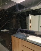 Czarne marmurowe ściany i blat umywalkowy z białymi żyłami w nowoczesnej łazience, oświetlenie punktowe w suficie, biała umywalka nablatowa i szafka z jasnego drewna.