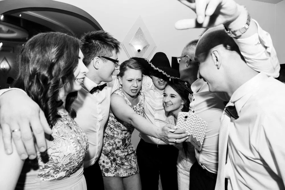 Czarno-białe zdjęcie grupy osób robiących sobie selfie na imprezie, jedna osoba w sombrero, różnorodne wyrazy twarzy.