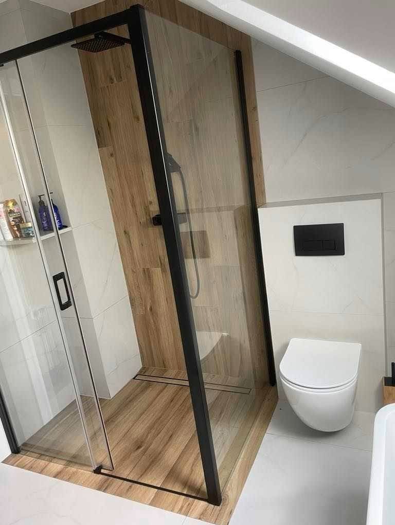 Nowoczesna łazienka z kabiną prysznicową typu walk-in z czarnymi profilami, drewnopodobną okładziną wewnątrz kabiny i białą ceramiką.