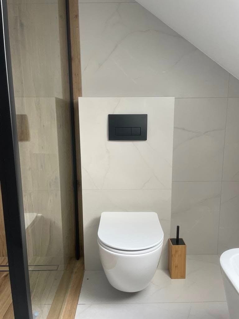 Nowoczesna, minimalistyczna łazienka w odcieniach bieli, z wiszącą toaletą i czarnym panelem sterującym spłuczką na ścianie, drewniany pojemnik na szczotkę toaletową.