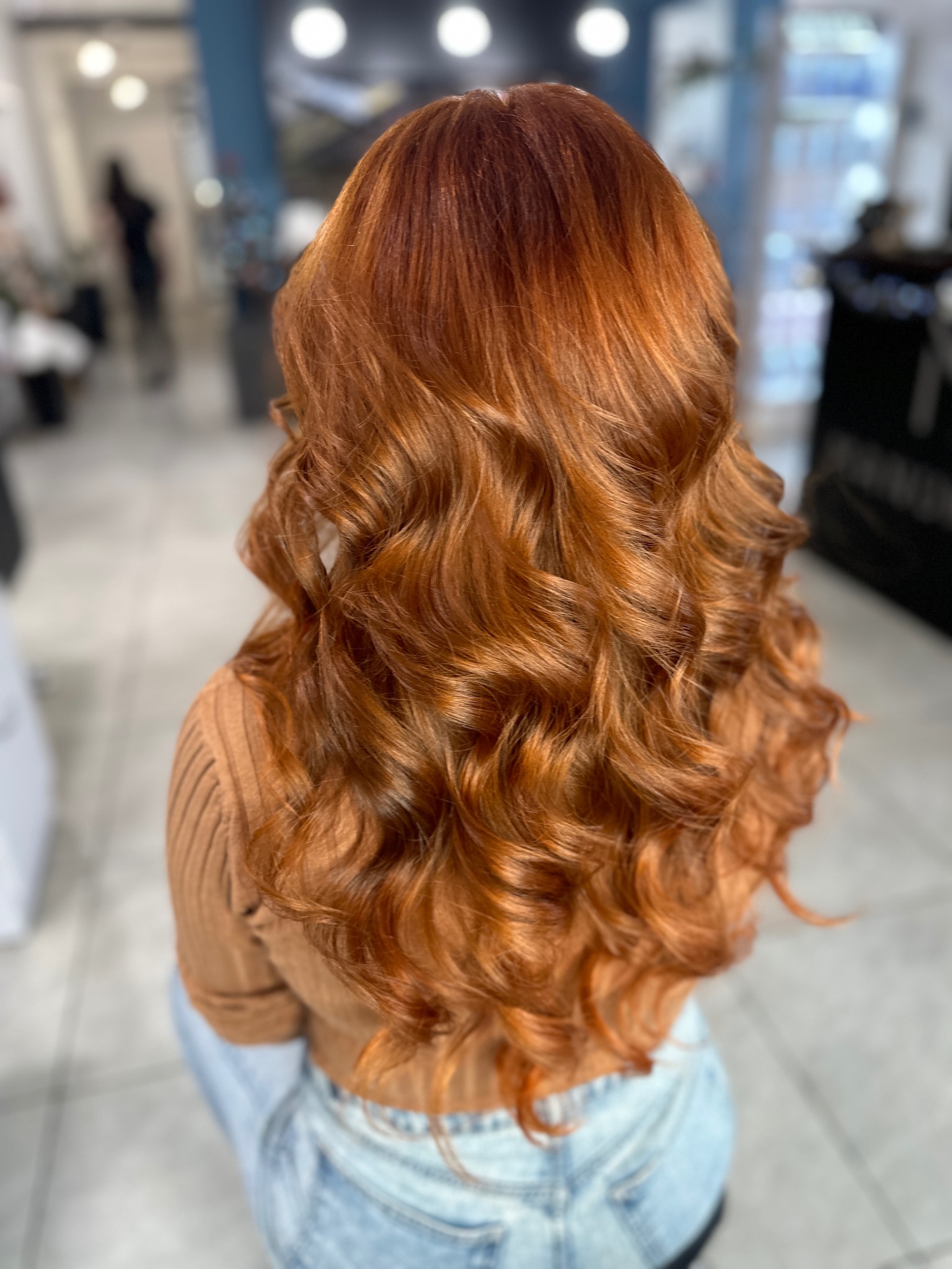 Długie, miedziane włosy z delikatnymi falami, widok z tyłu, na tle salonu fryzjerskiego.