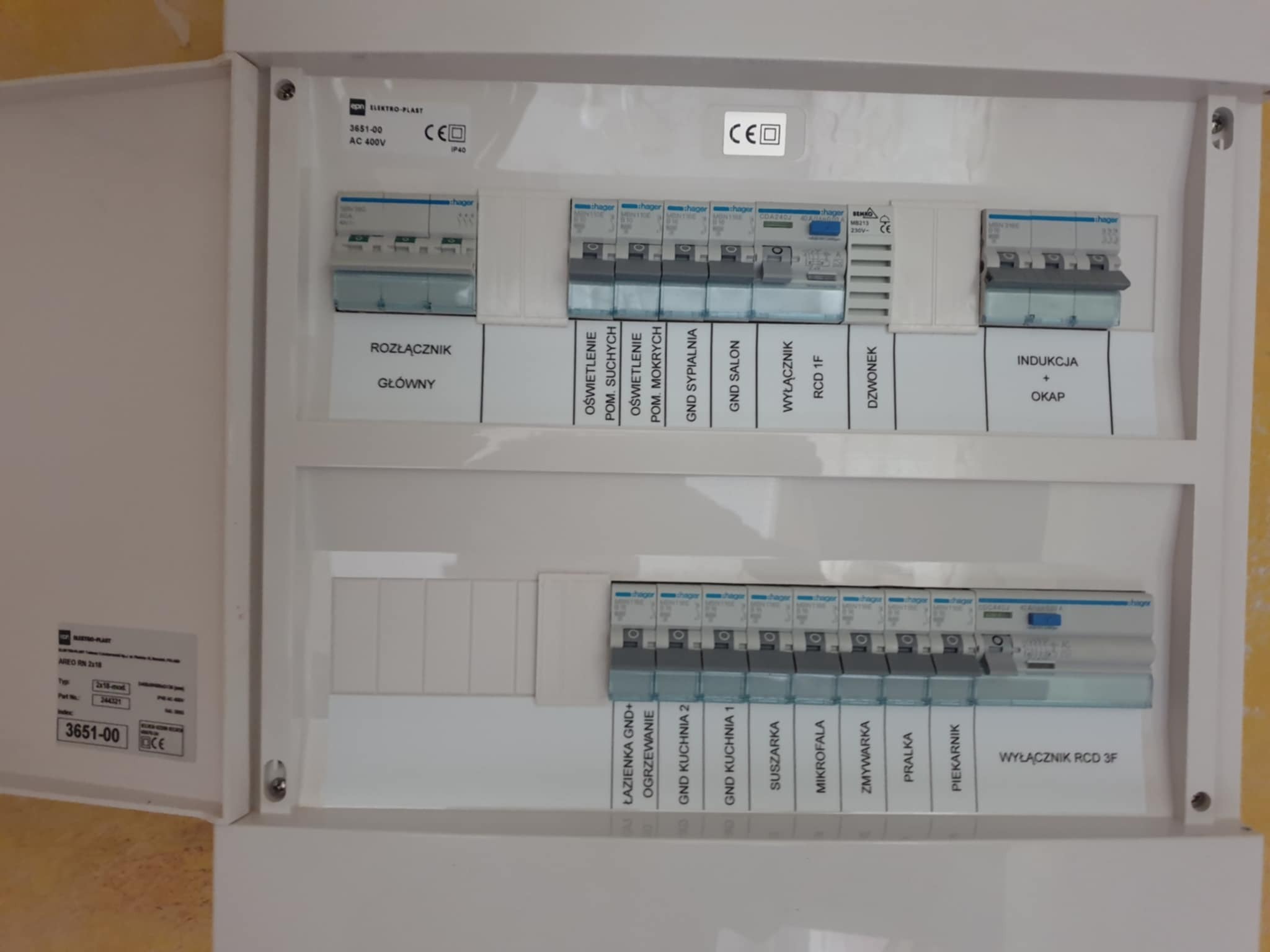 Rozdzielnia elektryczna z bezpiecznikami i opisami obwodów, widok z bliska na białą skrzynkę z zainstalowanymi elementami zabezpieczeń.